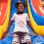 A boy smiling and mid-laugh at the bottom of a colorful inflatable slide.