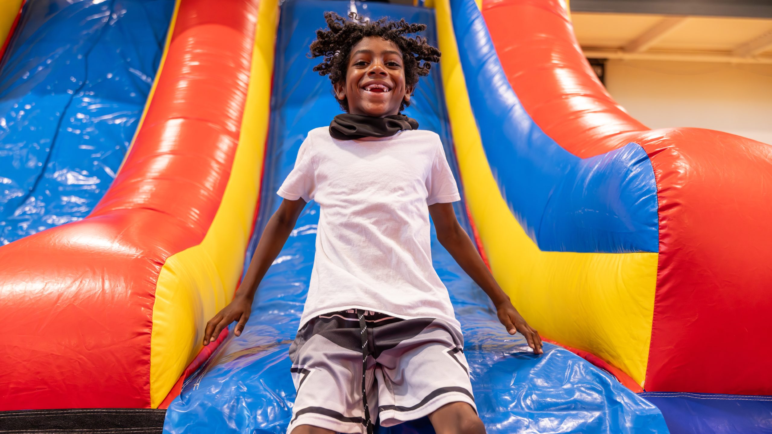 A boy smiling and mid-laugh at the bottom of a colorful inflatable slide.