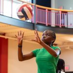 A girl in a green shirt looks up to set a volleyball on an indoor court.