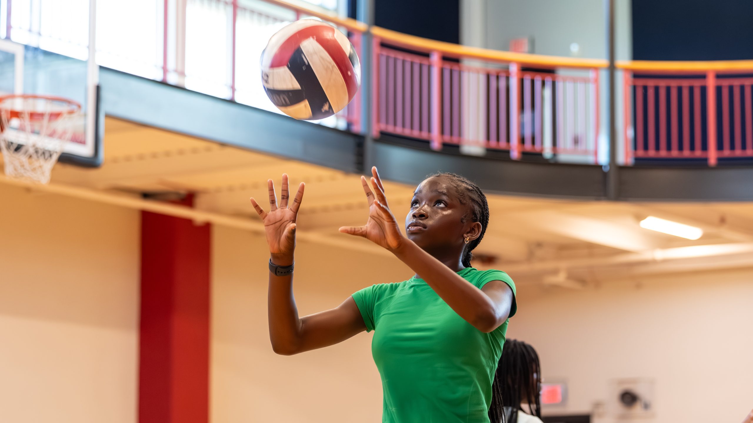 A girl in a green shirt looks up to set a volleyball on an indoor court.