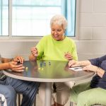 Three people smiling and sitting around a table rolling dice.