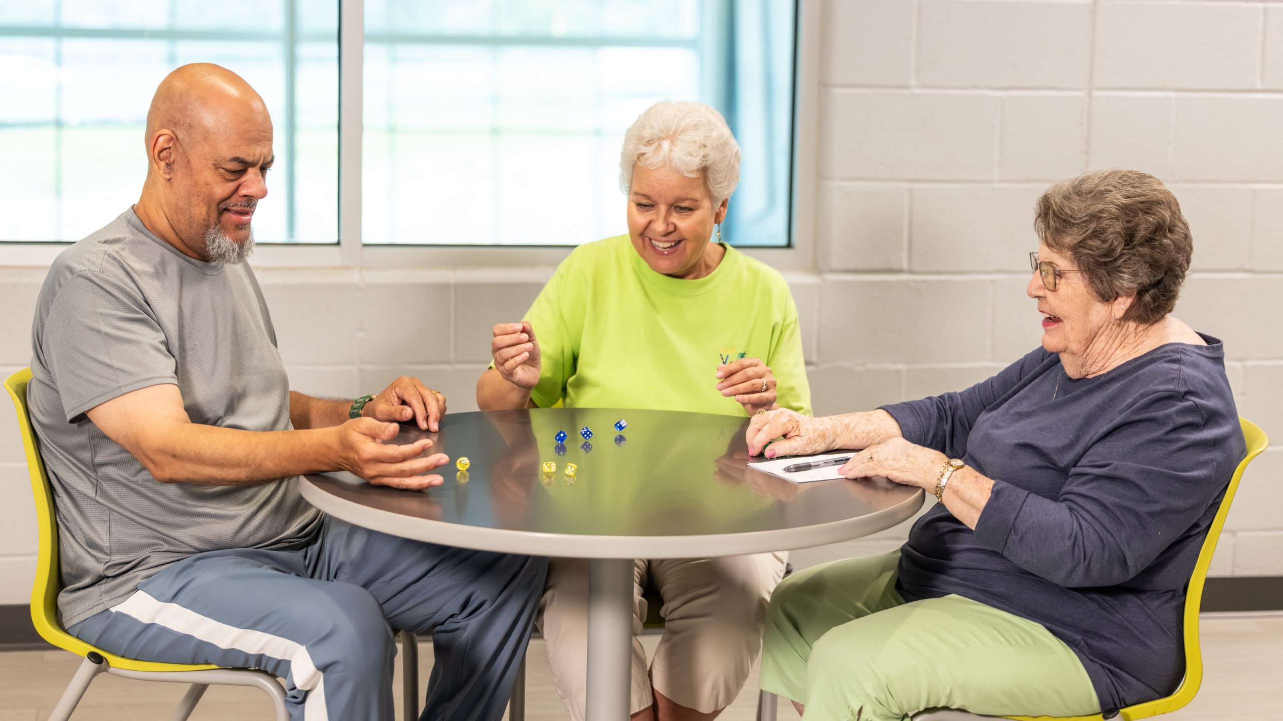Three people smiling and sitting around a table rolling dice.