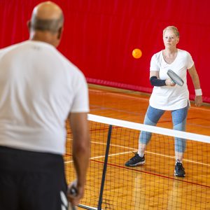A woman in a white shirt and blue leggings playing pickleball against a man in a white shirt and black pants at the REC Complex in Fairview Heights, IL.