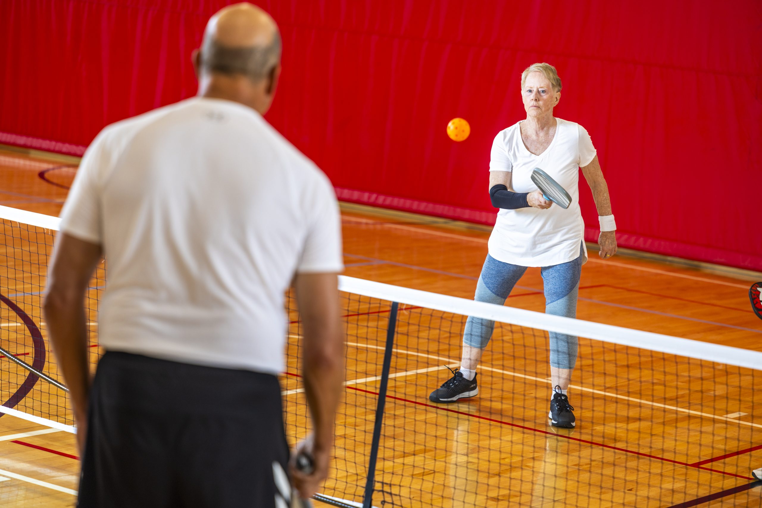 A woman in a white shirt and blue leggings playing pickleball against a man in a white shirt and black pants at the REC Complex in Fairview Heights, IL.