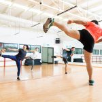 Full length of male instructor and clients kickboxing in dance class at gym.