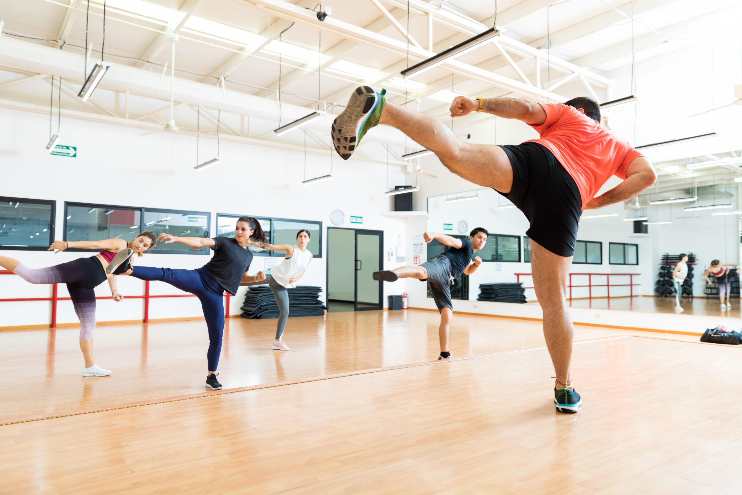 Full length of male instructor and clients kickboxing in dance class at gym.